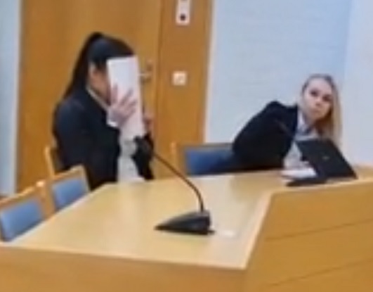 Kuvakaappaus harvinaisen huonolaatuiselta videolta. Väistöliikettä tekevä henkilö syytetyn oikealla puolella on tämän asianajaja Johanna Kenakkala-Kinnunen.