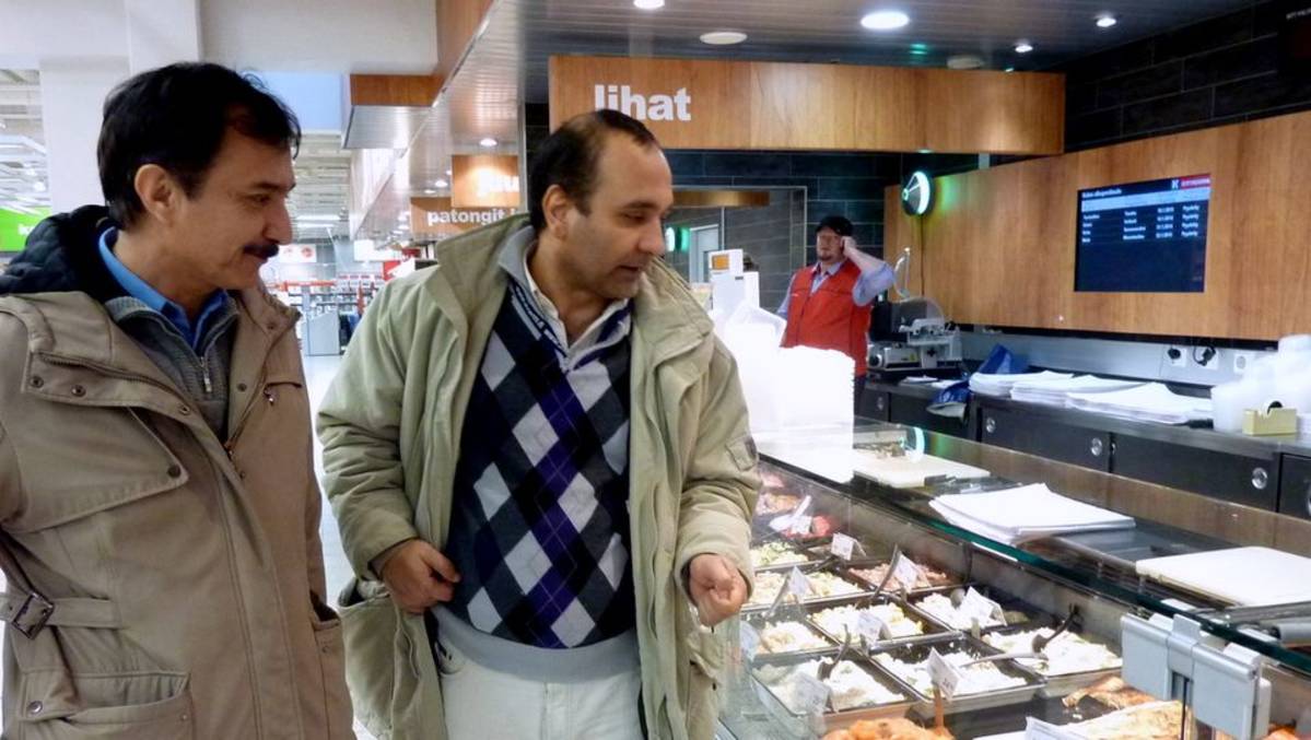 Ahmardjaad Hakim ja Ahmadshah Bayat tutkivat marketin valmisruokatiskissä missä kaikessa ruuassa on mukana porsaanlihaa. Taustalla lihamestari Jouni Luopajärvi.Yle / Sini Tanninen