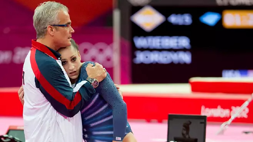 John Geddert (vas.) lohdutti yhdysvaltalaista voimistelijaa Jordyn Wieberiä Lontoon olympialaisissa vuonna 2012.jpg