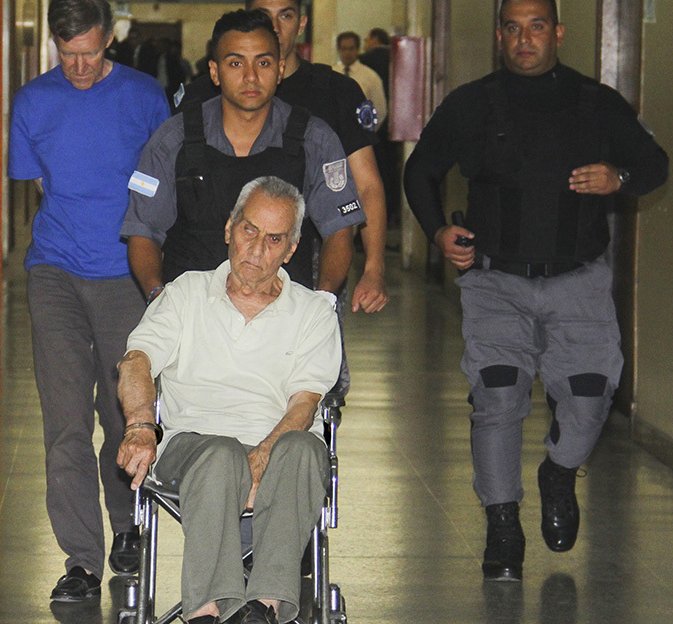 Nicola Corradi on kytketty pöyrätuoliin käsiraudoilla. Takana vasemmalla kävelee Horacio Corbacho.jpg
