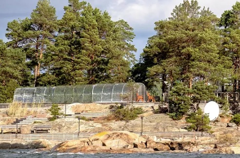 Säkkiluodolla on osittain naamioverkolla peitetty rakenne, joka muistuttaa kasvihuonetta. Vieressä on valvontakamera ja satelliittilautanen. (KUVA: KALLE KOPONEN / HS).