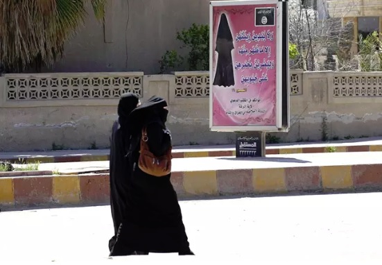 Naisia kulki Raqqassa maaliskuussa 2014 ohi julisteen, joka kehotti naisia verhoamaan itsensä. (KUVA: REUTERS)