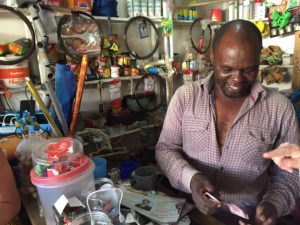 Arushalainen kioskiyrittäjä Hassan Yusuf Macha lataa aurinkoenergialla asiakkaidensa matkapuhelimia ja jäähdyttää pakastinta. Kylmästä juomasta voi veloittaa enemmän kuin lämpimästä.jpg
