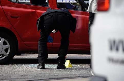 Rikostutkija poimi hylsyn läheltä punaista Toyotaa. Kuvassa näkyy myös murskaantunutta ikkunalasia. Havainnon mukaan ampuja hajotti ikkunan muuten kuin ampumalla. LUKIJAN KUVA